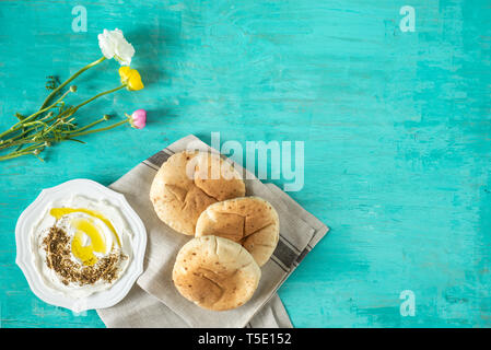 Labaneh labneh) des Mittleren Ostens soft Ziegenmilch Käse mit Olivenöl, Za'atar, Zitrone, Fladenbrot, am traditionellen Konzept auf rustikalen Holztisch serviert. Stockfoto