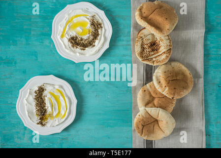 Labaneh labneh) des Mittleren Ostens soft Ziegenmilch Käse mit Olivenöl, Za'atar, Zitrone, Fladenbrot, am traditionellen Konzept über rustikal Tabl serviert. Stockfoto