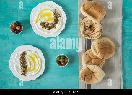 Labaneh labneh) des Mittleren Ostens soft Ziegenmilch Käse mit Olivenöl, Za'atar, Zitrone, Fladenbrot, am traditionellen Konzept über rustikal Tabl serviert. Stockfoto