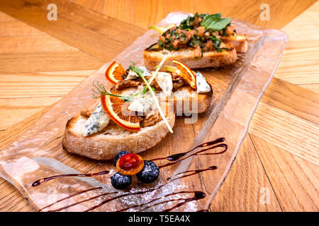 Vorspeise Bruschetta mit Käse, Honig, Nuss und Trocknen Orangenscheiben auf hölzernen Tisch. Stockfoto