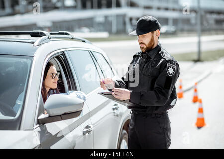 Polizist Dokumente prüfen einer jungen weiblichen Treiber stehen in der Nähe der Autos auf der Straße in der Stadt Stockfoto