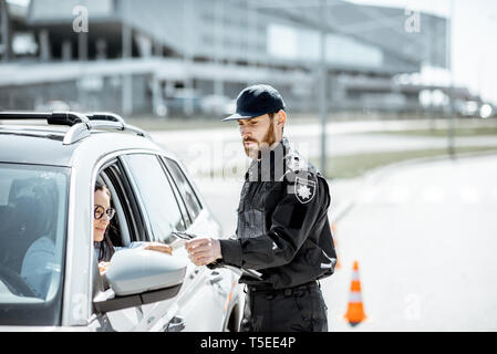 Polizist Dokumente prüfen einer jungen weiblichen Treiber stehen in der Nähe der Autos auf der Straße in der Stadt Stockfoto