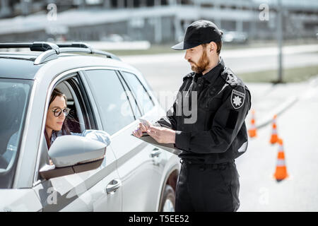 Polizist Dokumente prüfen einer jungen weiblichen Treiber stehen in der Nähe der Autos auf der Straße in der Stadt Stockfoto