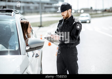 Polizist Dokumente prüfen einer jungen weiblichen Treiber stehen in der Nähe der Autos auf der Straße in der Stadt Stockfoto