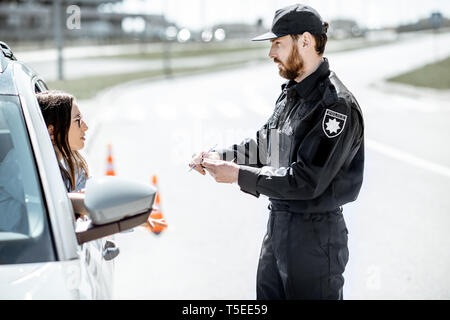 Polizist Dokumente prüfen einer jungen weiblichen Treiber stehen in der Nähe der Autos auf der Straße in der Stadt Stockfoto