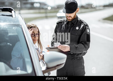 Polizist Dokumente prüfen einer jungen weiblichen Treiber stehen in der Nähe der Autos auf der Straße in der Stadt Stockfoto