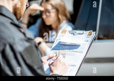 Polizist eine Geldstrafe für die Verletzung der Verkehrsregeln mit einer jungen Frau Treiber Blick auf den Ordner konzentriert Stockfoto