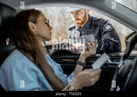 Polizist Dokumente prüfen einer jungen weiblichen Fahrer im Auto sitzen, Blick aus dem Innenraum Stockfoto