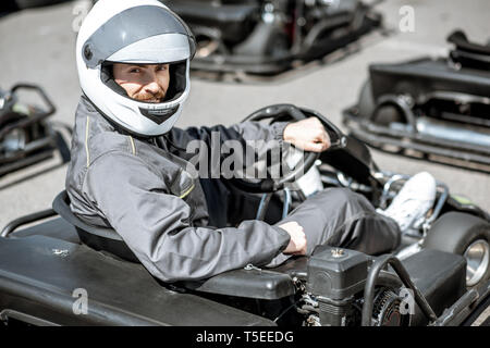 Porträt einer männlichen Racer in Sportkleidung und Protecive Helm sitzt in der Go-kart auf der Strecke im Freien Stockfoto