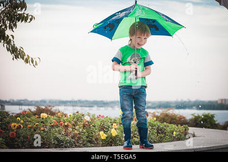 Lächelnde junge Holding einen Regenschirm unter Regen und Sonnenschein Stockfoto