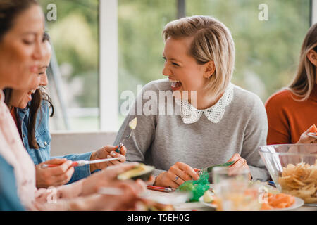 Kleine Gruppe von weiblichen Freunden an einem Tisch in einem Wintergarten zu sitzen. Sie bereiten Ihre Mittagessen, Sprechen und Lachen. Stockfoto