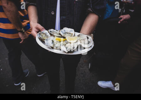 Mann Hand frische rohe Auster in paperr Platte mit Zitrone im Markt. Stockfoto