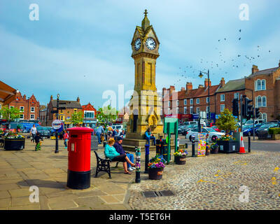 Die Stadt Wecker und einem hellen roten Briefkasten auf dem Markt mit Personen, die Frühlingssonne in Thirsk North Yorkshire UK Stockfoto