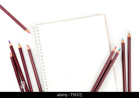 Ein Foto von einem shetchbook mit vielen verschiedenen Farbstifte um ihn herum, geschossen von oben auf einen weißen Hintergrund mit einem Platz für Text Stockfoto