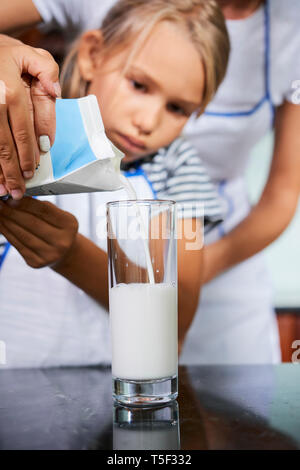 Mutter, Tochter Glas mit Milch zu füllen Stockfoto
