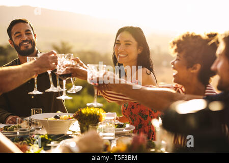 Eine Gruppe von Freunden einen Toast mit Getränken an der Partei. Junge Menschen an einem Tisch toasten Getränke und Abendessen zu genießen. Stockfoto