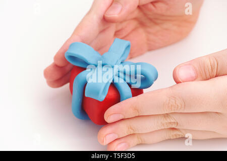 Junge hält Geschenk mit blauer Schleife umwickelt. Geringe Tiefenschärfe. Close Up. Geschenkbox und Band sind aus Lehm gemacht (Knetmasse). Stockfoto