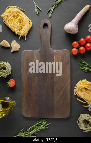 Schneidebrett und rohe pasta Tagliatelle, Tomaten, Rosmarin, Parmesan für die Küche Italienische Gerichte auf schwarzem Hintergrund. Platz für Text. Ansicht von oben Stockfoto