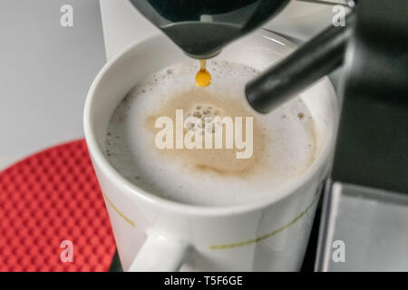 Die Cappuccino - Nahaufnahme von espresso Gießen aus der Kaffeemaschine. Cappuccino hat die wichtigsten Bestandteile sind Espresso, Milch. Unscharfer Hintergrund Stockfoto