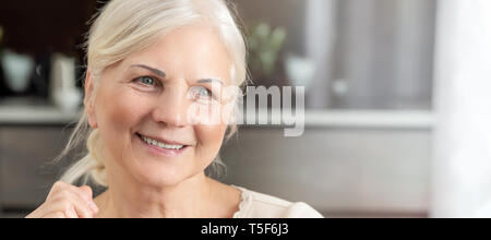 Freundliche ältere Frau Porträt. Rentner Frau sitzt zu Hause und schaut zum Fenster. Konzept einer glücklichen Ruhestand Stockfoto