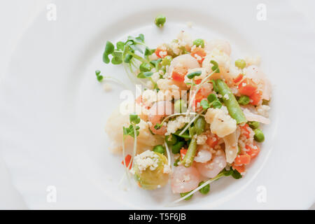 Couscous mit Gemüse, Garnelen und Radieschen auf einem weißen Teller Stockfoto
