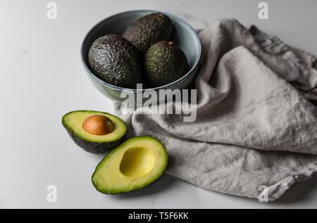 Schüssel mit Avocados mit einem Schnitt in der Hälfte auf weißem Marmor Arbeitsplatte. Stockfoto