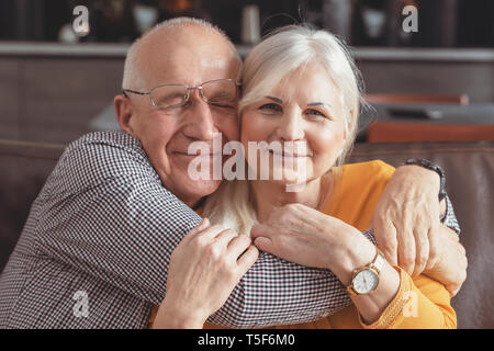 Fröhliche, romantische senior Paar umarmen beim Sitzen auf dem Sofa zu Hause Stockfoto