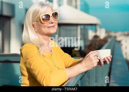 Freundliche, ältere Frau genießt sonnigen Tag auf dem Balkon. Ältere Leute Aktivität auf Ruhestand Konzept Stockfoto