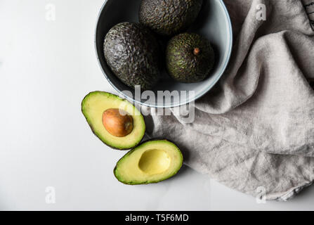 Schüssel mit Avocados mit einem Schnitt in der Hälfte auf einem weißen Arbeitsplatte. Stockfoto