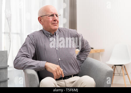 Ältere Menschen leiden unter Rückenschmerzen sitzen auf einem Sessel zu Hause Stockfoto
