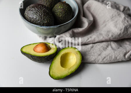 Schüssel mit Avocados mit einem Schnitt in der Hälfte auf einem weißen Arbeitsplatte. Stockfoto