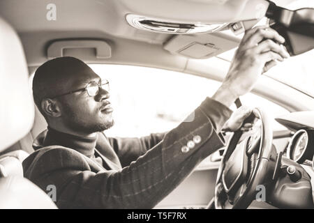 Ein junger Geschäftsmann im Anzug hinter dem Steuer eines teuren Auto sitzen passt ein Rückspiegel. Stockfoto