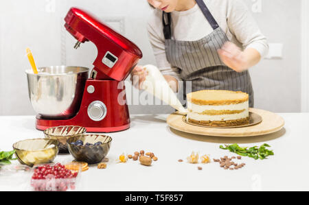 Junge weibliche Konditor peitschen Speiseeis in einer Metallschüssel im Roten elektrischen Mixer. Das Konzept der hausgemachte Kuchen, Kochen. Stockfoto