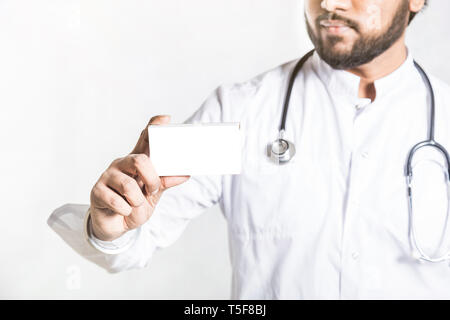 Hübscher junger Arzt in einem weißen Mantel mit einem Stethoskop hält auf der ausgestreckten Hand einen leeren weißen Karton für die Blister Paket von Pillen. Mock up. Stockfoto