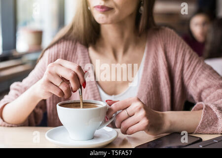 Schöne junge Frau sitzt an einem Tisch in einem Café bei einer Tasse Kaffee und schaut aus dem Fenster Stockfoto