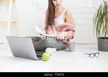 Junge Frau sitzt auf dem Boden in einem skandinavischen apartment Interieur mit einem Laptop, Studium der Rechtswissenschaften, freiberufliche Mädchen bei der Arbeit, Distance Learning student Stockfoto