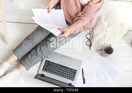 Eine junge Frau sitzt auf dem Boden in einem hellen Wohnung oder Büro innen und arbeitet an einem Laptop, Freelancer Mädchen bei der Arbeit, das Konzept der Abstand Stockfoto