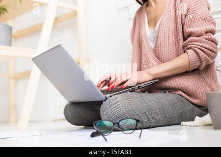 Eine junge Frau sitzt auf dem Boden in einem hellen Wohnung oder Büro innen und arbeitet an einem Laptop, Freelancer Mädchen bei der Arbeit, das Konzept der Abstand Stockfoto