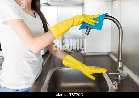 Eine junge Frau in gelb Handschuhe wäscht Kran mit einem Schwamm in der Spüle. Haus professionelle Reinigung Stockfoto