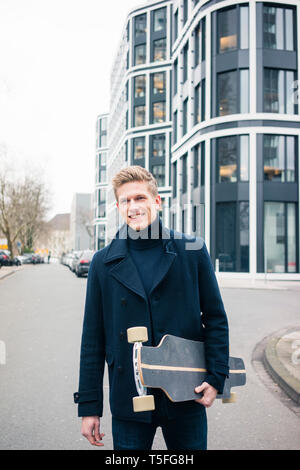 Portrait von lächelnden jungen Mann mit Skateboard in der Stadt Stockfoto