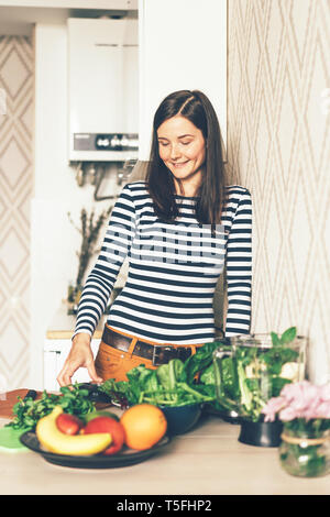 Junge stilvolle hipster Frau in das Innere ihrer Küche, im Vordergrund Grüns und Gemüse, gesunde Lebensmittel Stockfoto