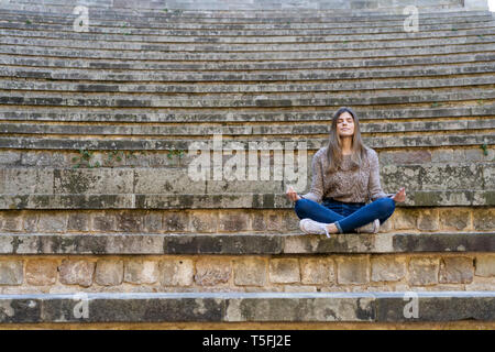 Junge Frau sitzt im Freien auf Treppen Yoga Stockfoto