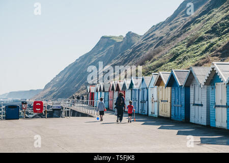 Sheringham, Großbritannien - 21 April, 2019: Frau mit zwei Kindern, zu Fuß durch die bunten Badekabinen am Meer in Sheringham an einem sonnigen Tag. Sheringham ist ein Englischer Stockfoto