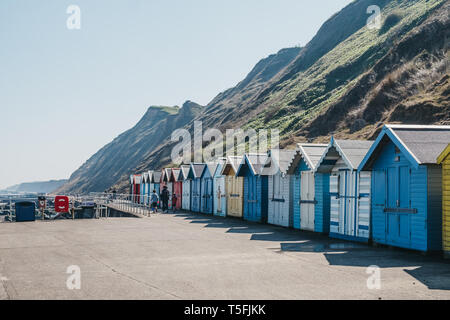 Sheringham, Großbritannien - 21 April, 2019: Menschen zu Fuß von bunten Badekabinen am Meer in Sheringham an einem sonnigen Tag. Sheringham ist eine englische Stadt am Meer Stockfoto