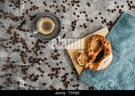Tasse schwarzen Kaffee, Kaffeebohnen und Brezel auf Serviette und Holzbrett Stockfoto