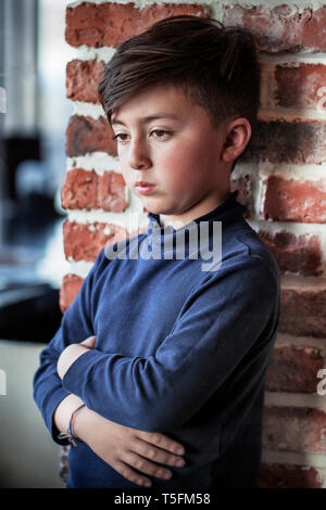 Gemischte Rasse asiatischen Kaukasischen Jungen mit gekreuzten Armen trägt blaue Rolli vor Red brick wall Stockfoto