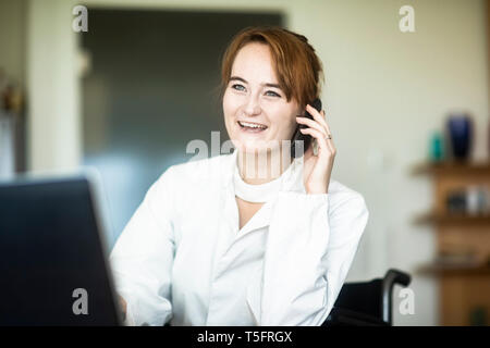 Portrait von lächelnden jungen Arzt im Rollstuhl auf dem Telefon Stockfoto