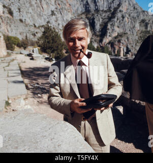 Joachim Fuchsberger zieht ein thunfischwadenfänger Pfeife, welche vorher er aus seiner Tasche geholt hatte, in den Ruinen von Delphi, Griechenland 1970er. Joachim Fuchsberger zieht an seiner Pfeife, die Er vorher aus der Tasche genommen hatte, zu den Ruinen von Delphi, Griechenland 1970 s Stockfoto