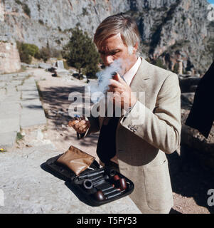 Joachim Fuchsberger zieht ein thunfischwadenfänger Pfeife, welche vorher er aus seiner Tasche geholt hatte, in den Ruinen von Delphi, Griechenland 1970er. Joachim Fuchsberger zieht an seiner Pfeife, die Er vorher aus der Tasche genommen hatte, zu den Ruinen von Delphi, Griechenland 1970 s Stockfoto