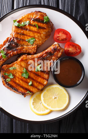 Lecker Gegrilltes Schweinesteak in einer würzigen Tamarind Sauce, mit Zitrone und frischen Tomaten closeup auf einem Teller auf den Tisch. Vertikal oben Ansicht von oben Stockfoto